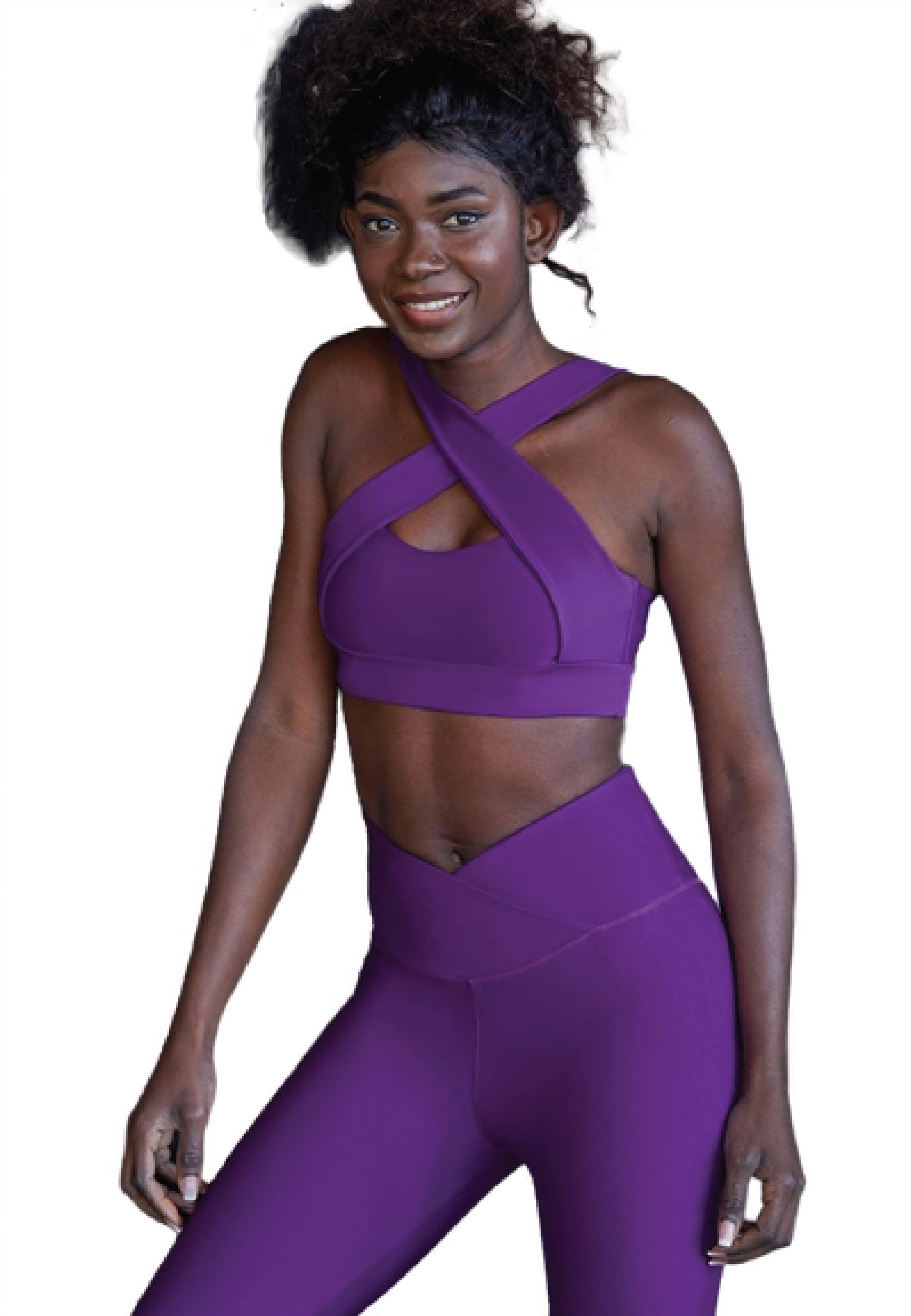 Person in einem lila Criss-Cross-Sport-BH und Violett-Lismina-Leggings, lächelt vor einem weißen Hintergrund.